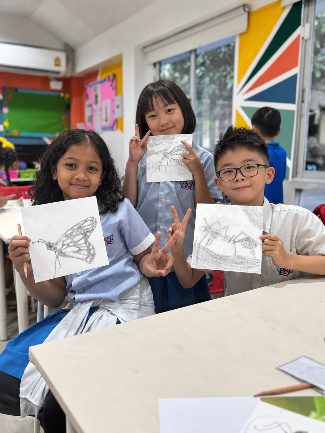 Students holding up their pencil sketches of insects and butterflies