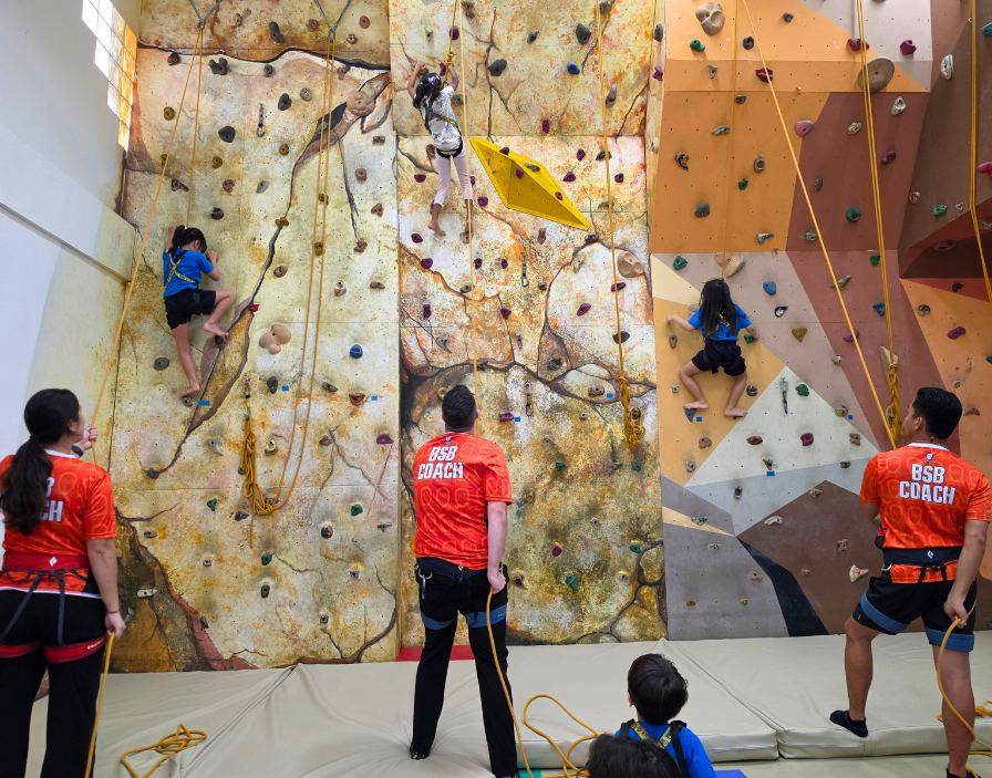 Students climbing the wall with coaches during Climbing Club