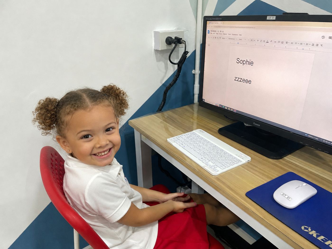 A young student smiling at her computer during a typing activity