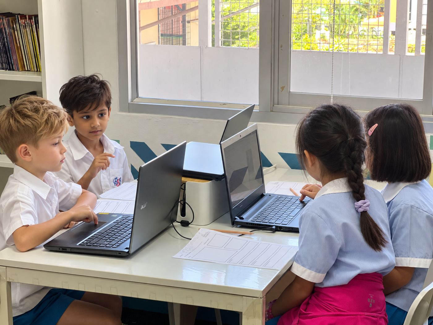 Students working together on laptops by the window during research time