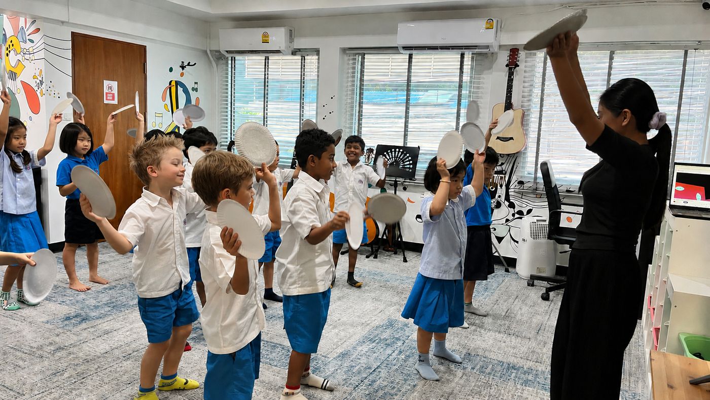 Students holding paper plates as cymbals during a rhythm activity with their teacher