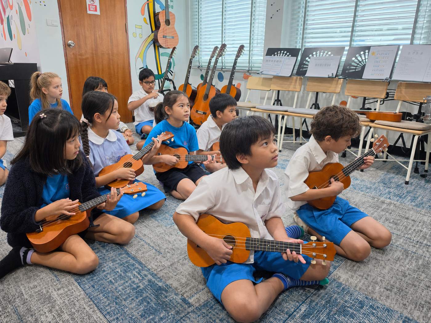 A group of students sitting cross-legged playing ukuleles together