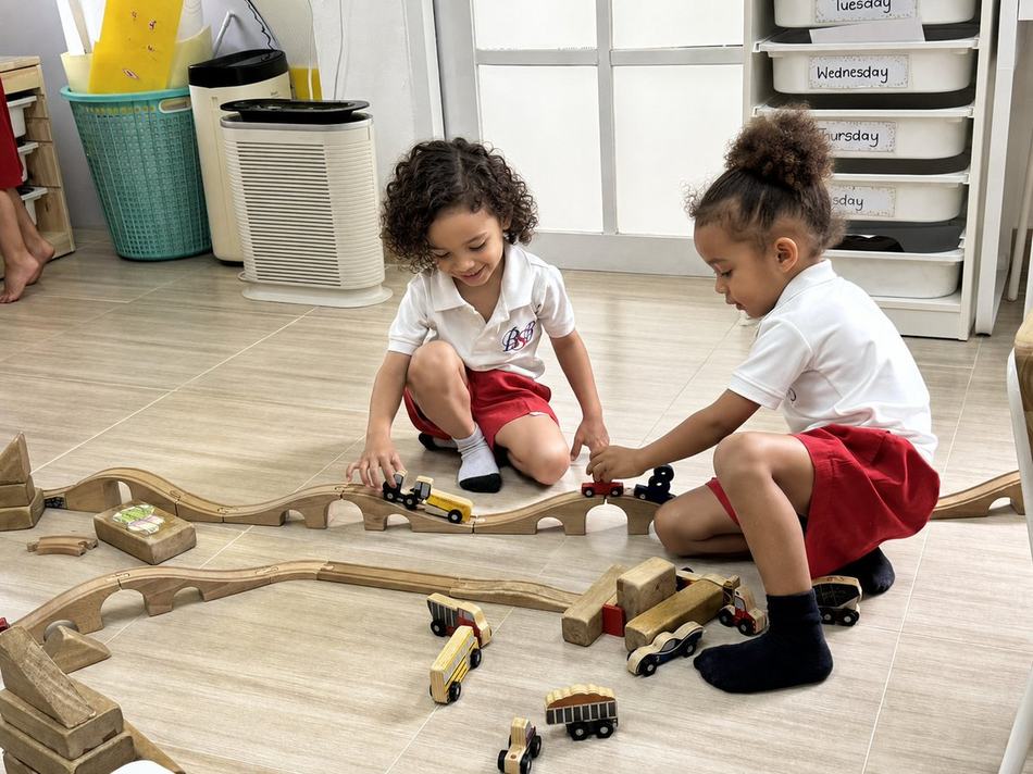 Two students playing together with a wooden train track