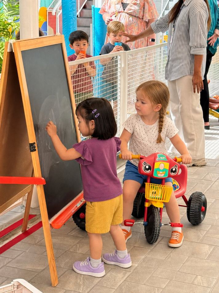 Students drawing on a chalkboard and riding a tricycle together