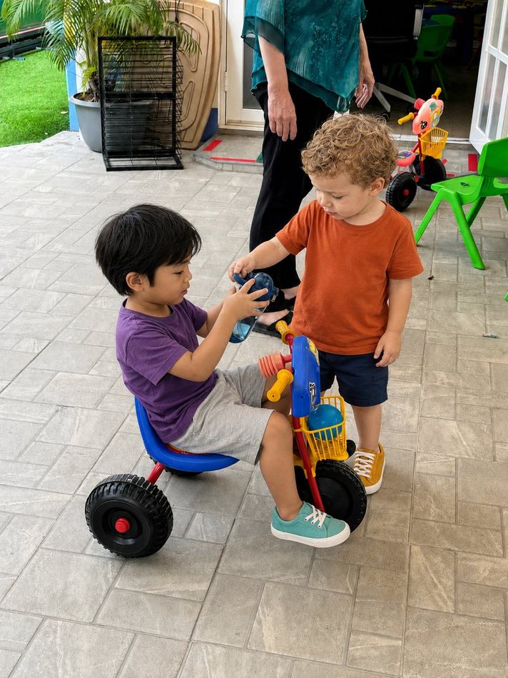 Students sharing a drink while playing with a tricycle outdoors