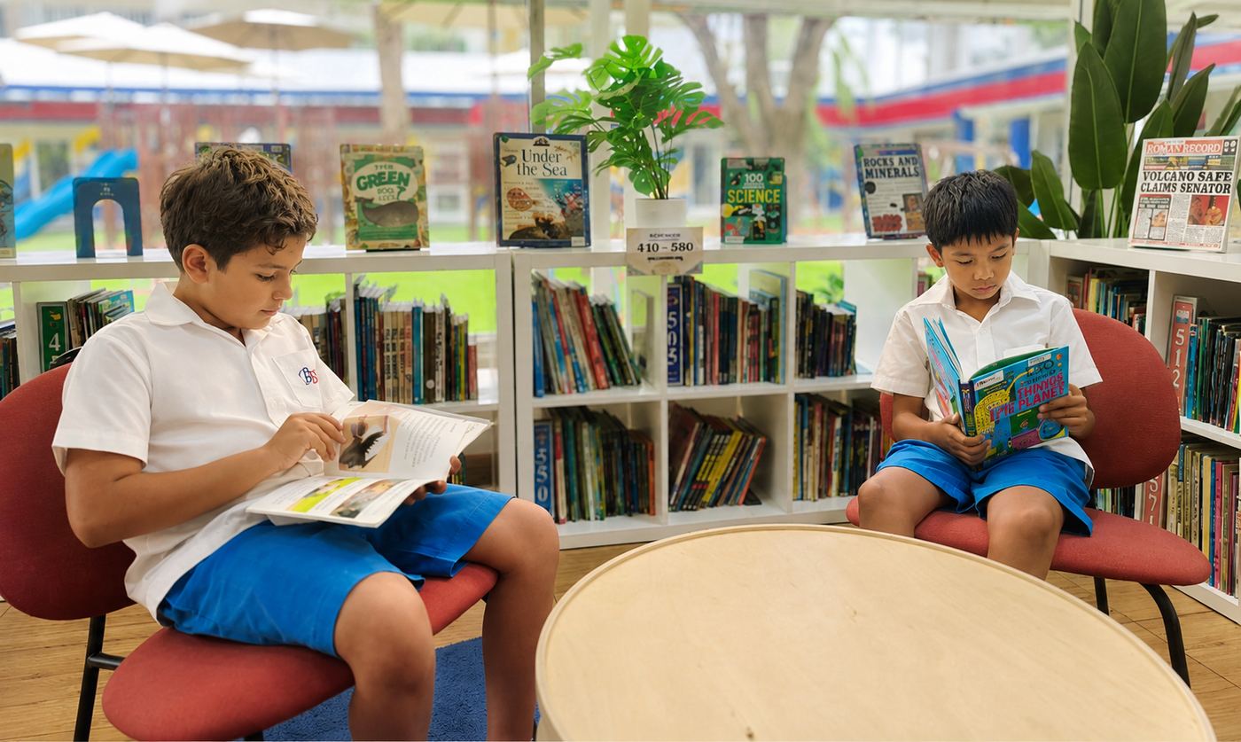 Two students reading together by the library windows
